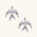 White gold-plated bird earrings with spread wings and oval zirconia center on cream background