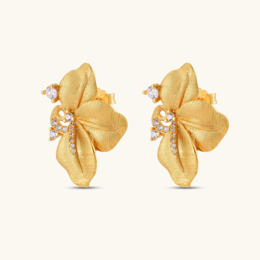 Gold-plated 925 silver flower stud earrings with brushed finish, swirl detail, and pavé cubic zirconia on cream background.