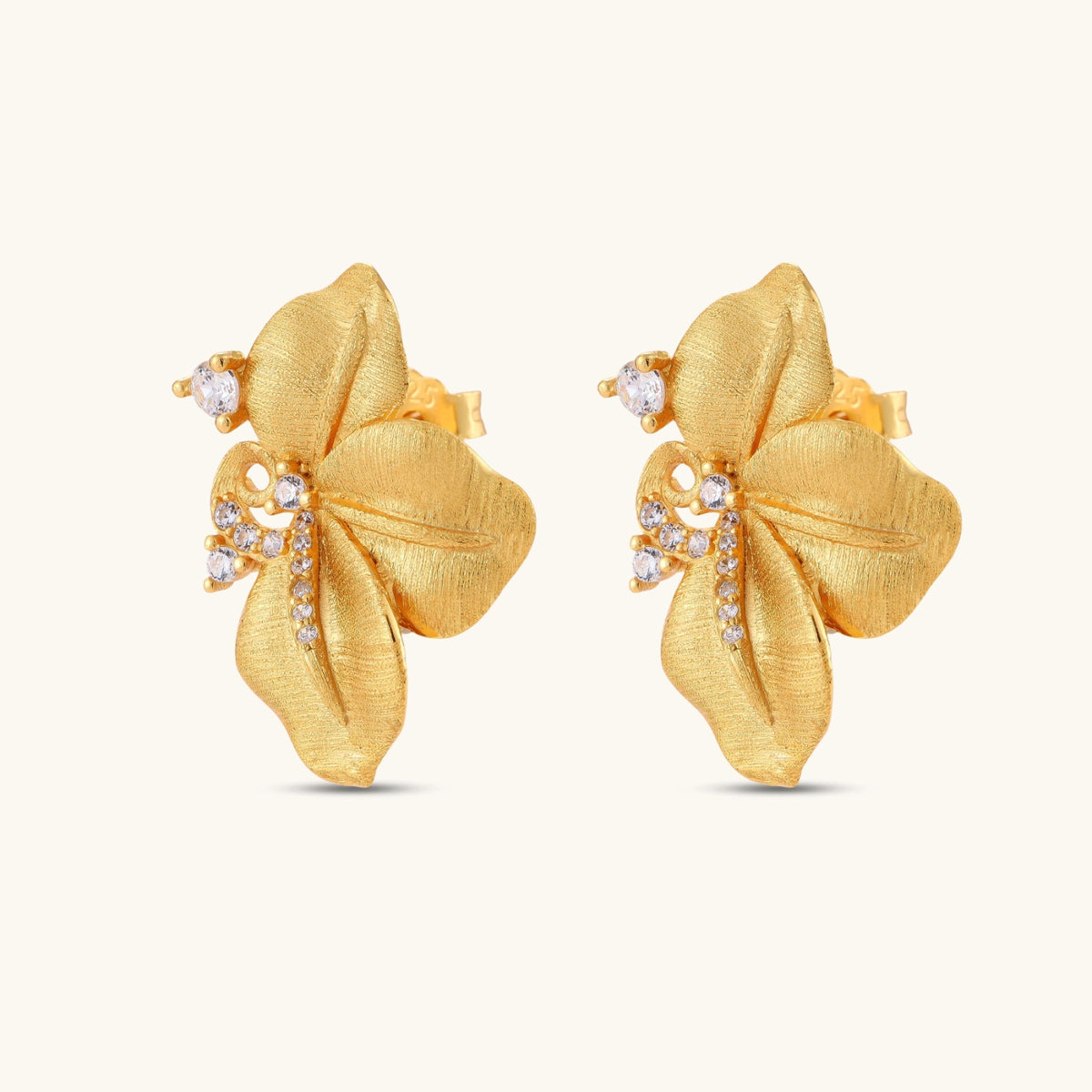 Gold-plated 925 silver flower stud earrings with brushed finish, swirl detail, and pavé cubic zirconia on cream background.