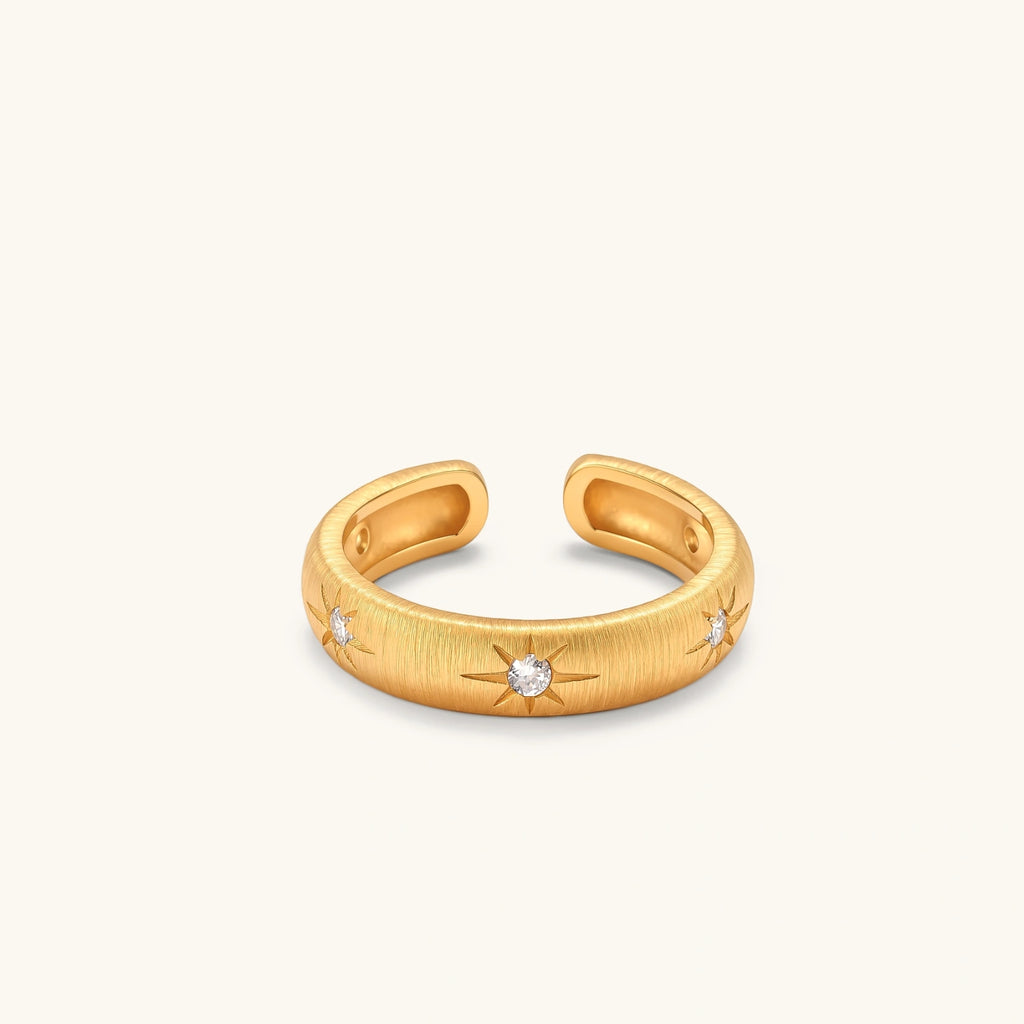 Gold open-band cuff ring with brushed matte finish, engraved 8-point star motifs, and round CZ stones on white background.