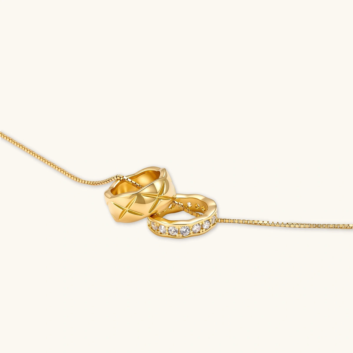 Gold box-chain necklace with two interlocking ring pendants — one star-engraved, one pavé cubic zirconia, 18K gold-plated.